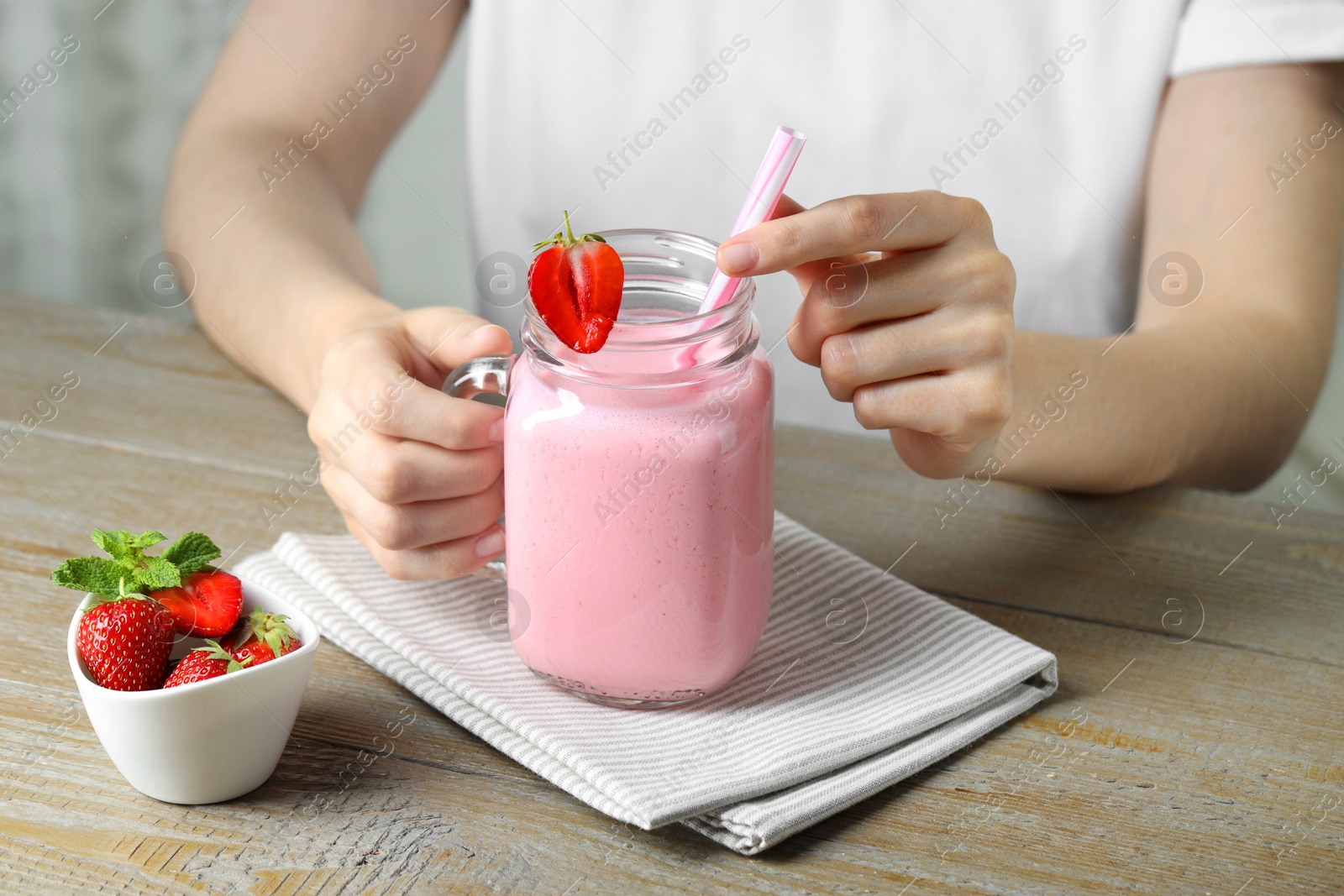 Photo of Woman with mason jar of tasty strawberry yogurt at wooden table, closeup