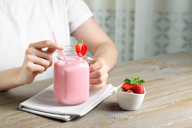 Photo of Woman with mason jar of tasty strawberry yogurt at wooden table, closeup