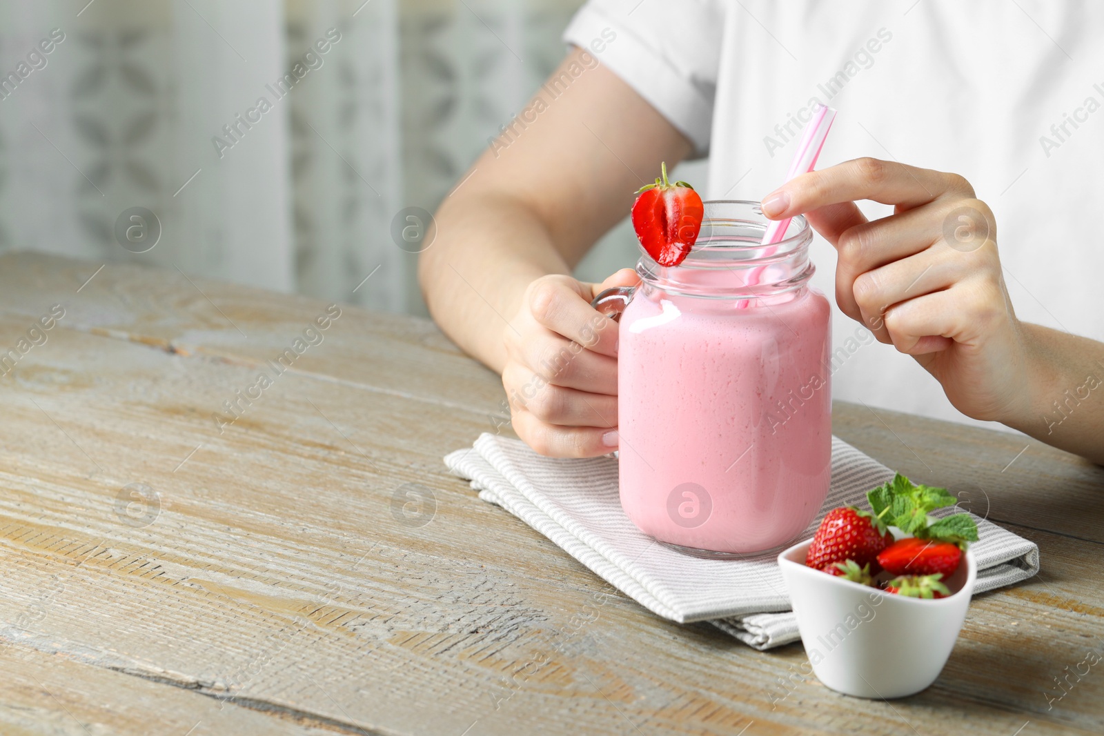 Photo of Woman with mason jar of tasty strawberry yogurt at wooden table, closeup. Space for text