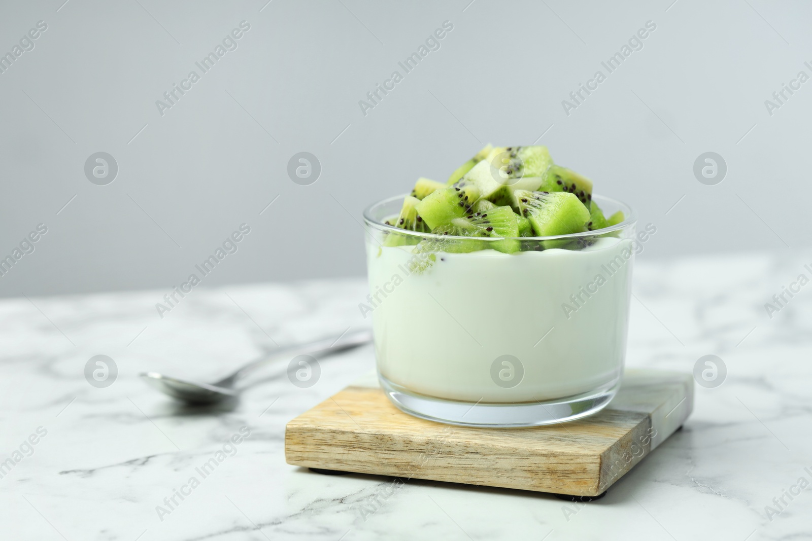 Photo of Tasty yogurt with fresh kiwi in glass on white marble table, space for text