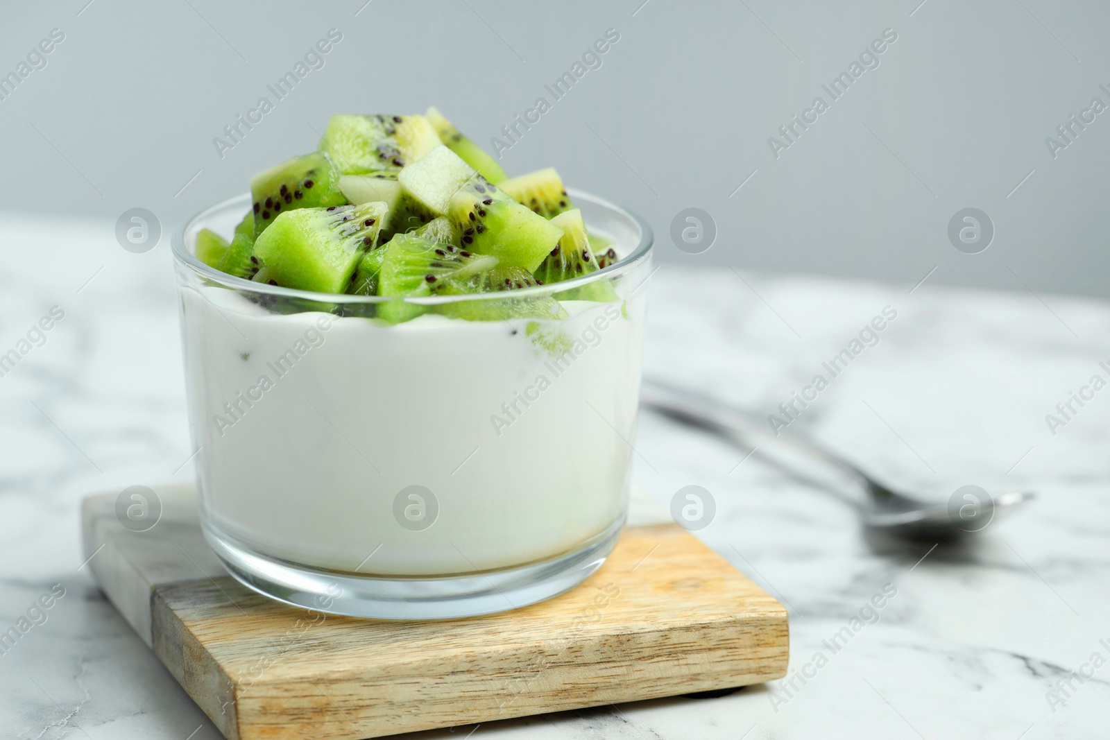 Photo of Tasty yogurt with fresh kiwi in glass on white marble table, closeup