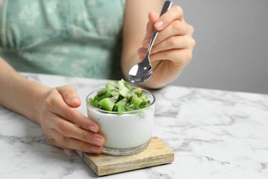 Woman eating tasty yogurt with fresh kiwi at white marble table, closeup. Space for text