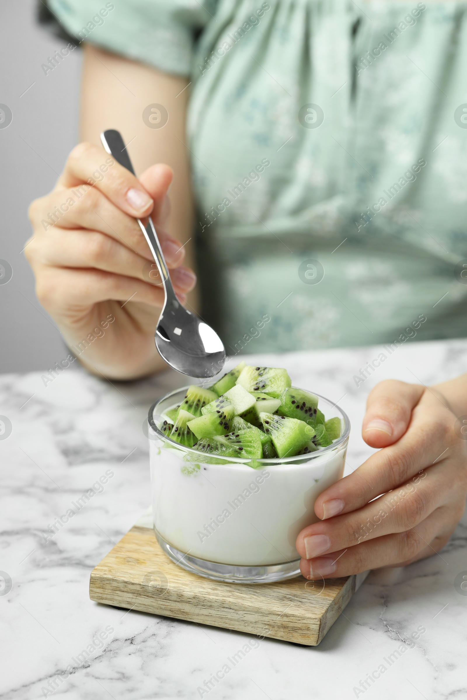 Photo of Woman eating tasty yogurt with fresh kiwi at white marble table, closeup