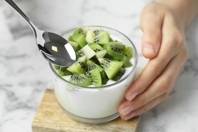 Photo of Woman eating tasty yogurt with fresh kiwi at light table, closeup