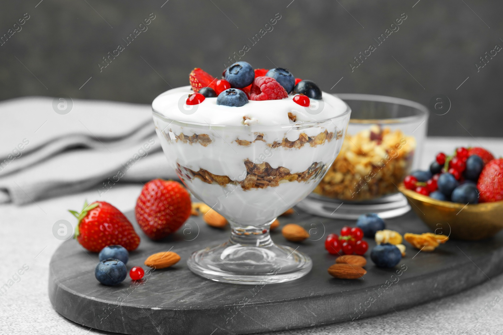 Photo of Tasty yogurt with fresh berries, granola and nuts on gray table, closeup