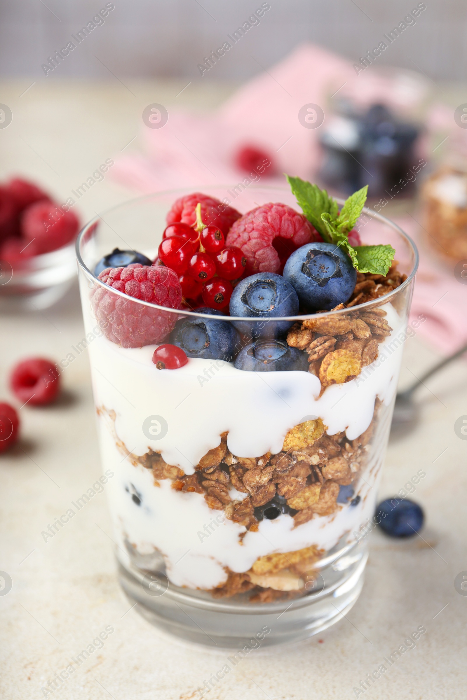 Photo of Tasty yogurt with fresh berries, granola and mint in glass on gray textured table, closeup