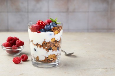 Tasty yogurt with fresh berries, granola and mint in glass on gray textured table, space for text