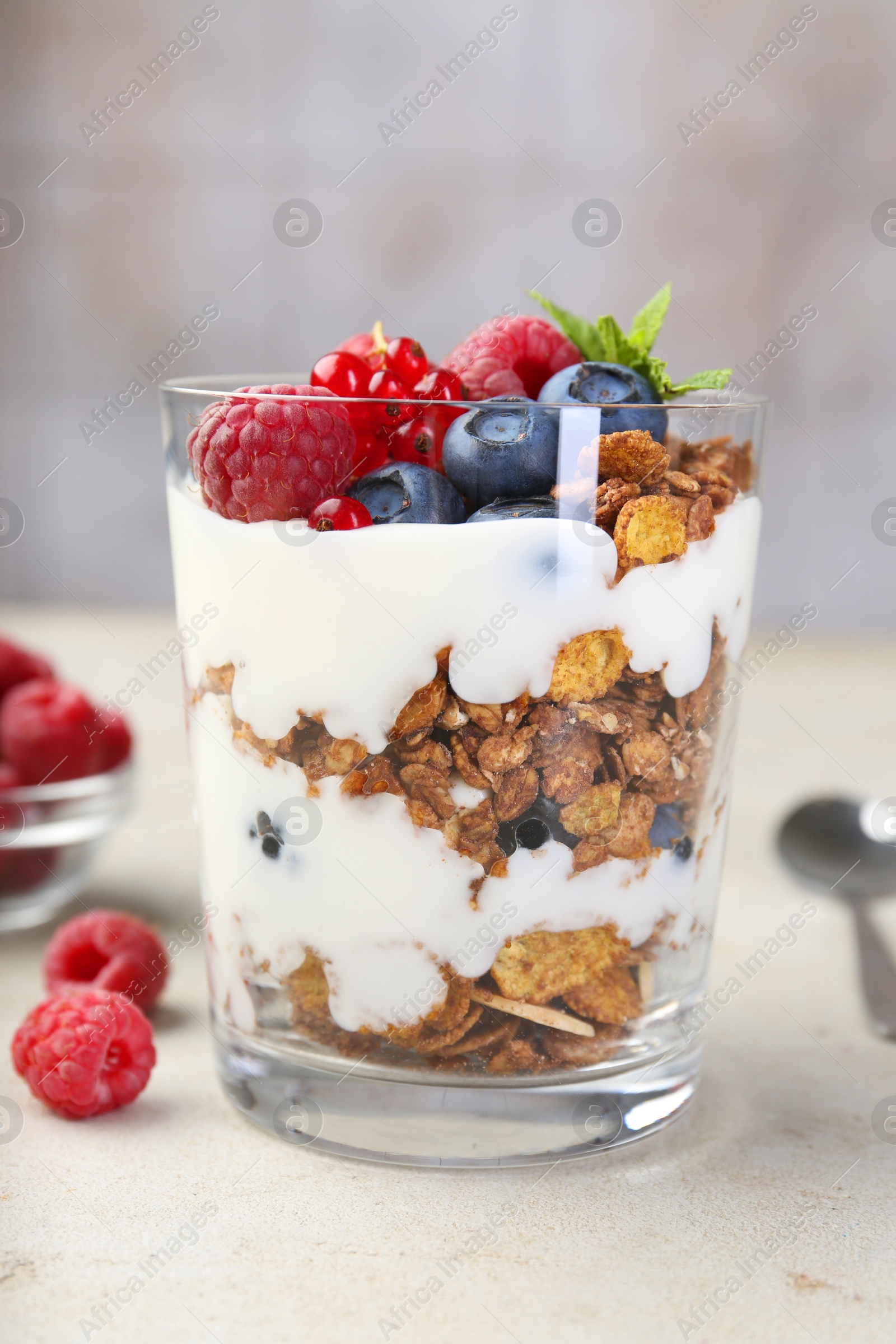 Photo of Tasty yogurt with fresh berries, granola and mint in glass on gray textured table