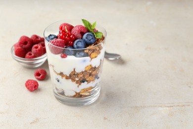 Photo of Tasty yogurt with fresh berries, granola and mint in glass on gray textured table, space for text