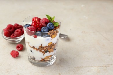 Tasty yogurt with fresh berries, granola and mint in glass on gray textured table, space for text