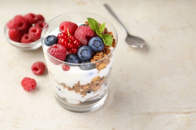 Photo of Tasty yogurt with fresh berries, granola and mint in glass on gray textured table, closeup. Space for text