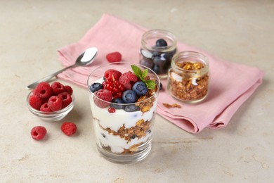 Photo of Tasty yogurt with fresh berries, granola and mint in glass on gray textured table