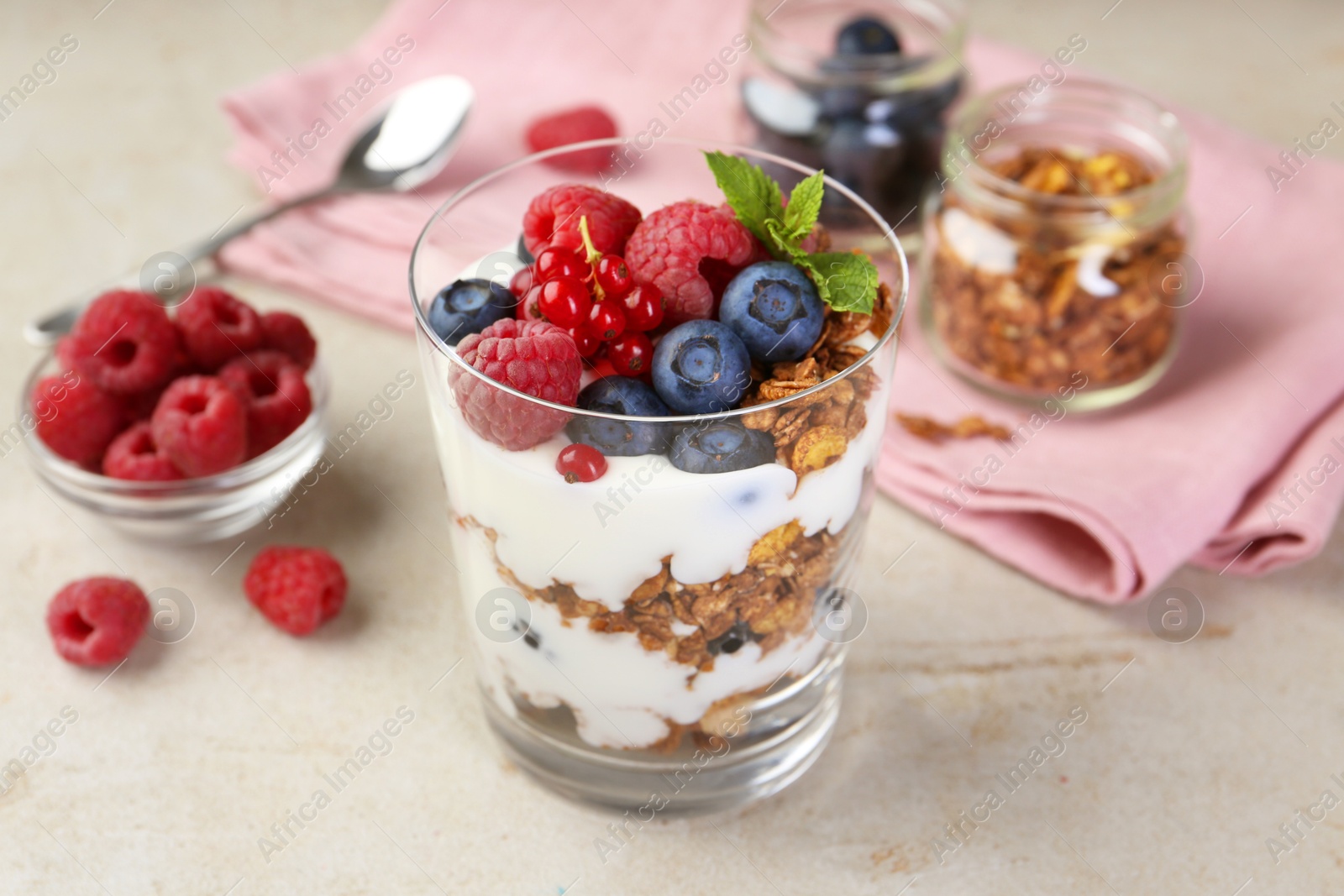 Photo of Tasty yogurt with fresh berries, granola and mint in glass on gray textured table, closeup