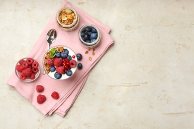 Photo of Tasty yogurt with fresh berries, granola, mint in glass and spoon on gray textured table, flat lay. Space for text