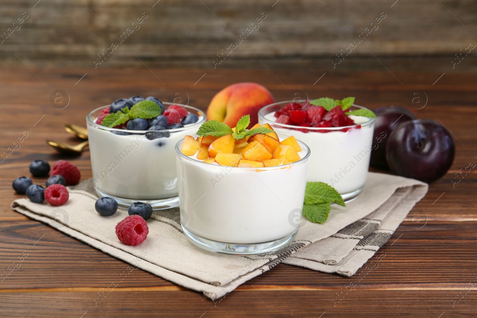 Photo of Tasty yogurt with fresh berries, fruits and mint in glasses on wooden table, closeup