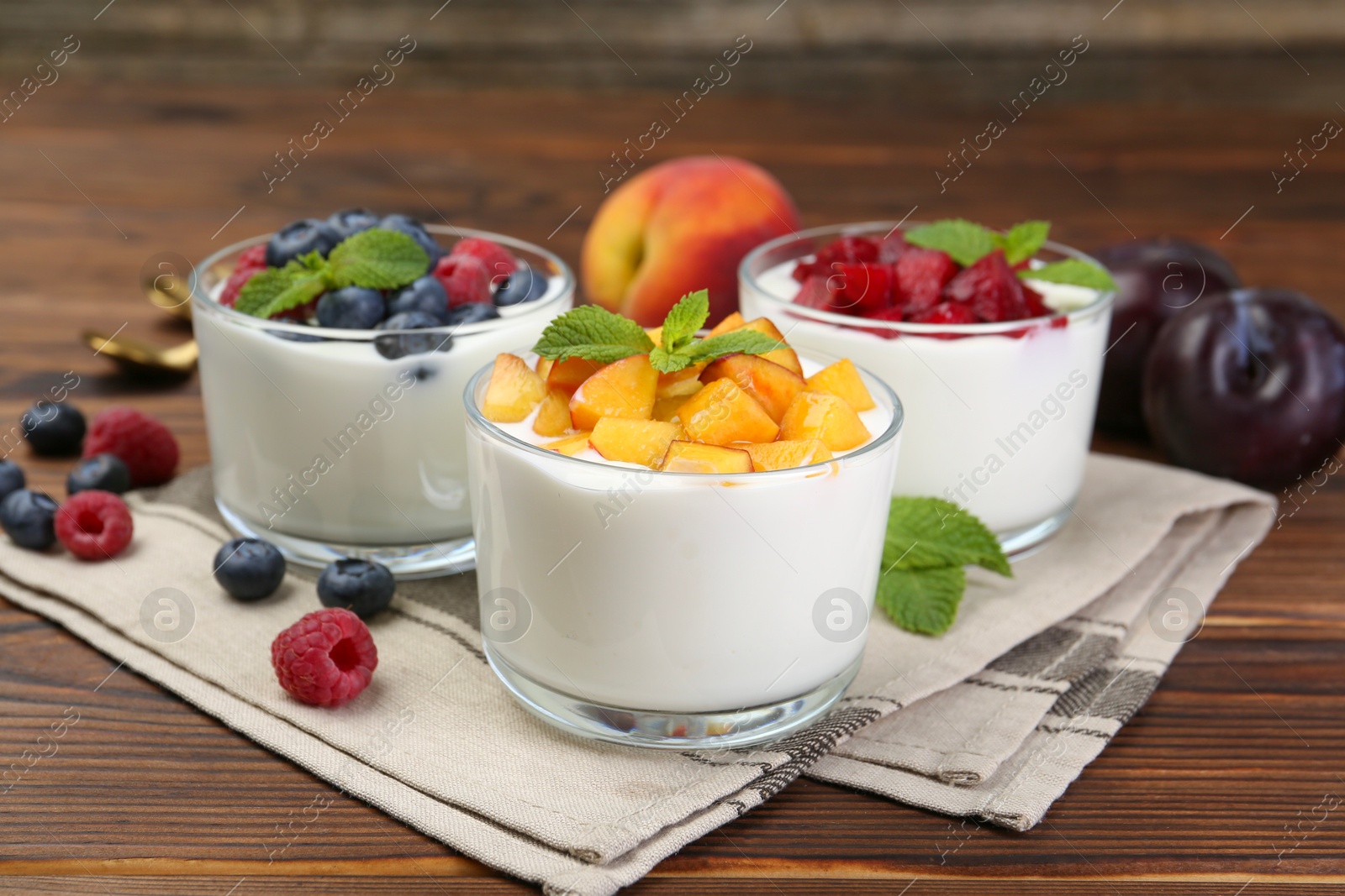 Photo of Tasty yogurt with fresh berries, fruits and mint in glasses on wooden table, closeup