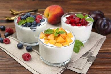 Photo of Tasty yogurt with fresh berries, fruits and mint in glasses on wooden table, closeup