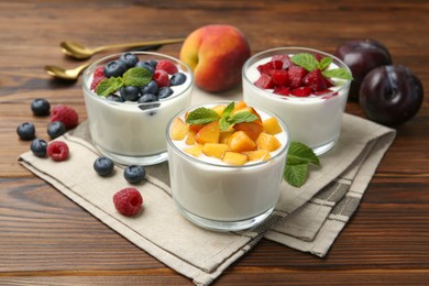 Photo of Tasty yogurt with fresh berries, fruits and mint in glasses on wooden table, closeup