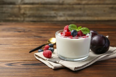 Tasty yogurt with fresh plums, berries and mint in glass on wooden table, space for text