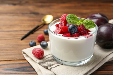 Tasty yogurt with fresh plums, berries and mint in glass on wooden table, space for text