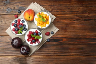 Photo of Tasty yogurt with fresh berries, fruits and mint in glasses on wooden table, flat lay. Space for text