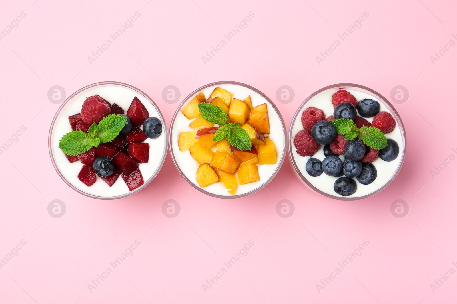 Photo of Tasty yogurt with fresh berries, fruits and mint in glasses on pink background, top view