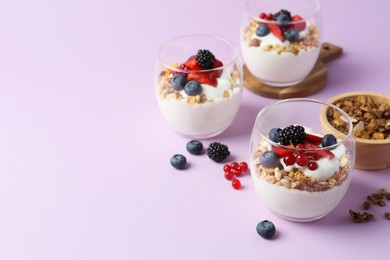 Photo of Tasty yogurt with fresh berries and granola in glasses on violet background, space for text