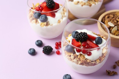 Photo of Tasty yogurt with fresh berries and granola in glasses on violet background, closeup