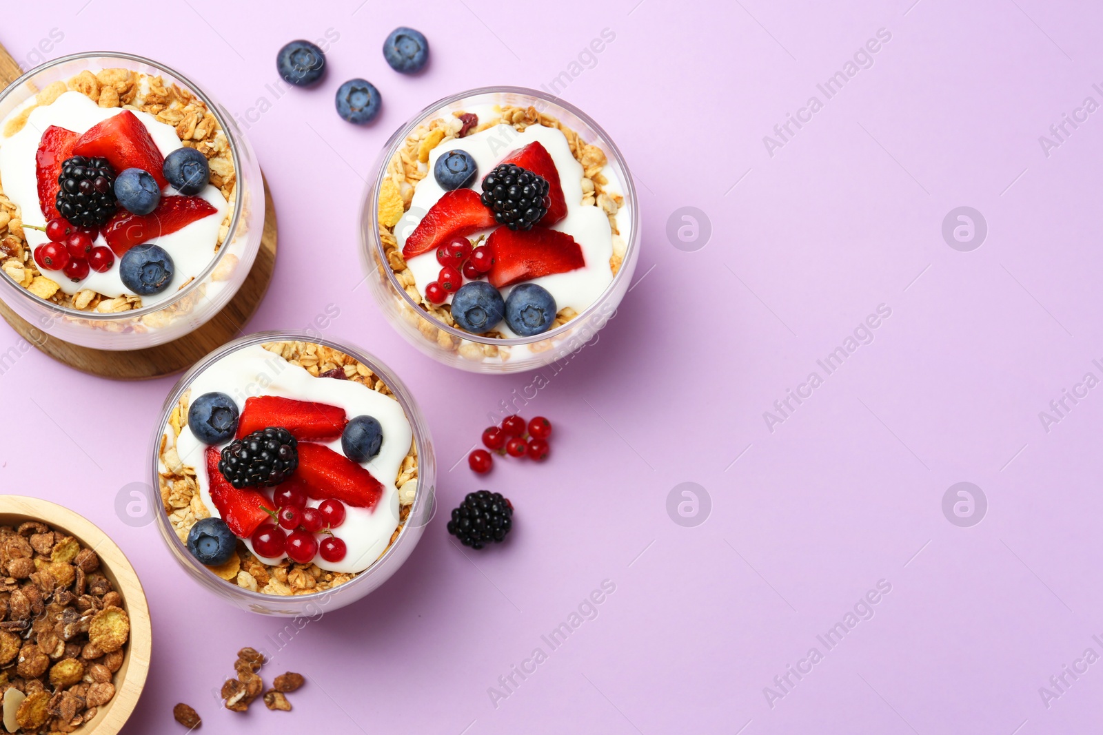 Photo of Tasty yogurt with fresh berries and granola in glasses on violet background, flat lay. Space for text