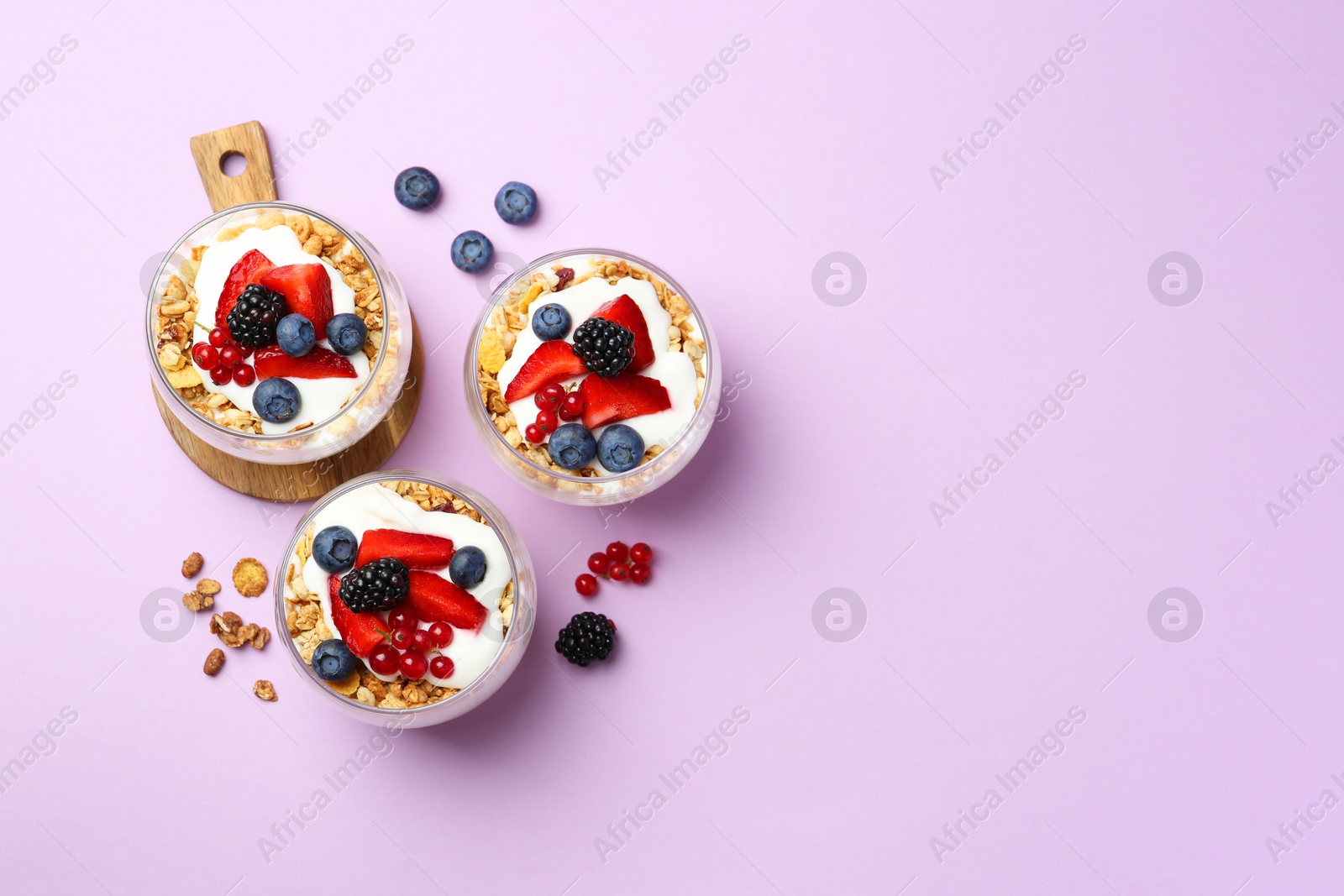 Photo of Tasty yogurt with fresh berries and granola in glasses on violet background, flat lay. Space for text