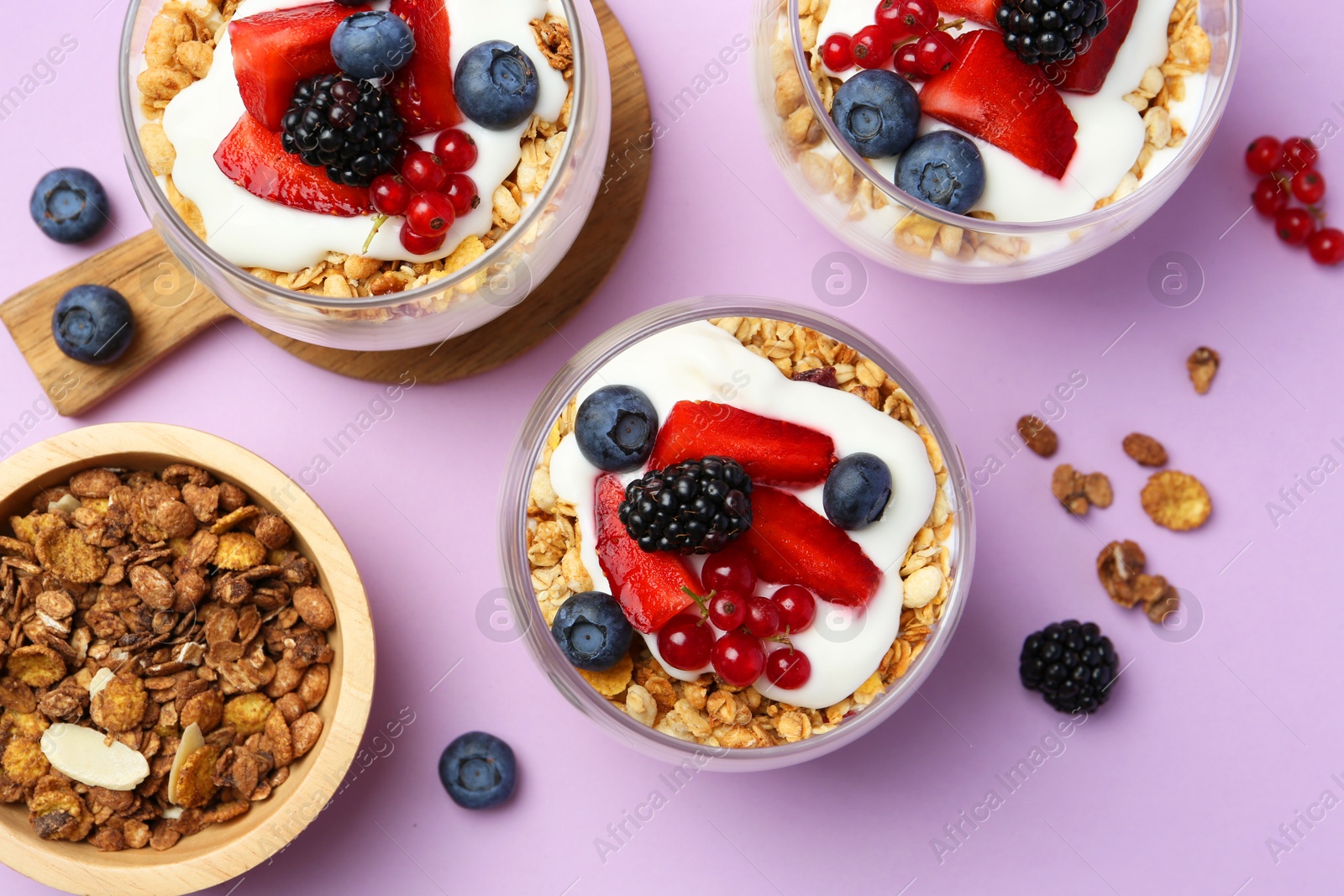 Photo of Tasty yogurt with fresh berries and granola in glasses on violet background, flat lay