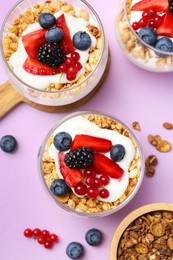 Photo of Tasty yogurt with fresh berries and granola in glasses on violet background, flat lay