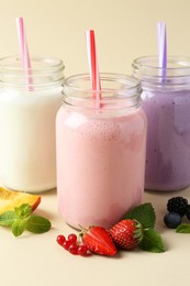 Different tasty yogurts in mason jars, peach, fresh berries and mint on pale yellow background, closeup