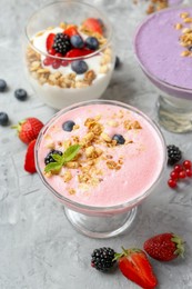 Photo of Different tasty yogurts with fresh berries and granola in glass dessert bowls on gray textured table, closeup