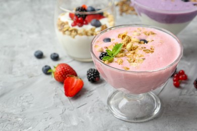 Photo of Different tasty yogurts with fresh berries and granola in glass dessert bowls on gray textured table, closeup