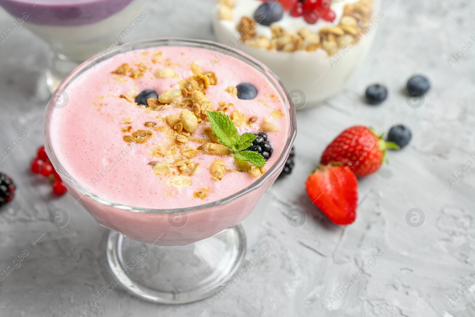 Photo of Different tasty yogurts with fresh berries and granola in glass dessert bowls on gray textured table, closeup