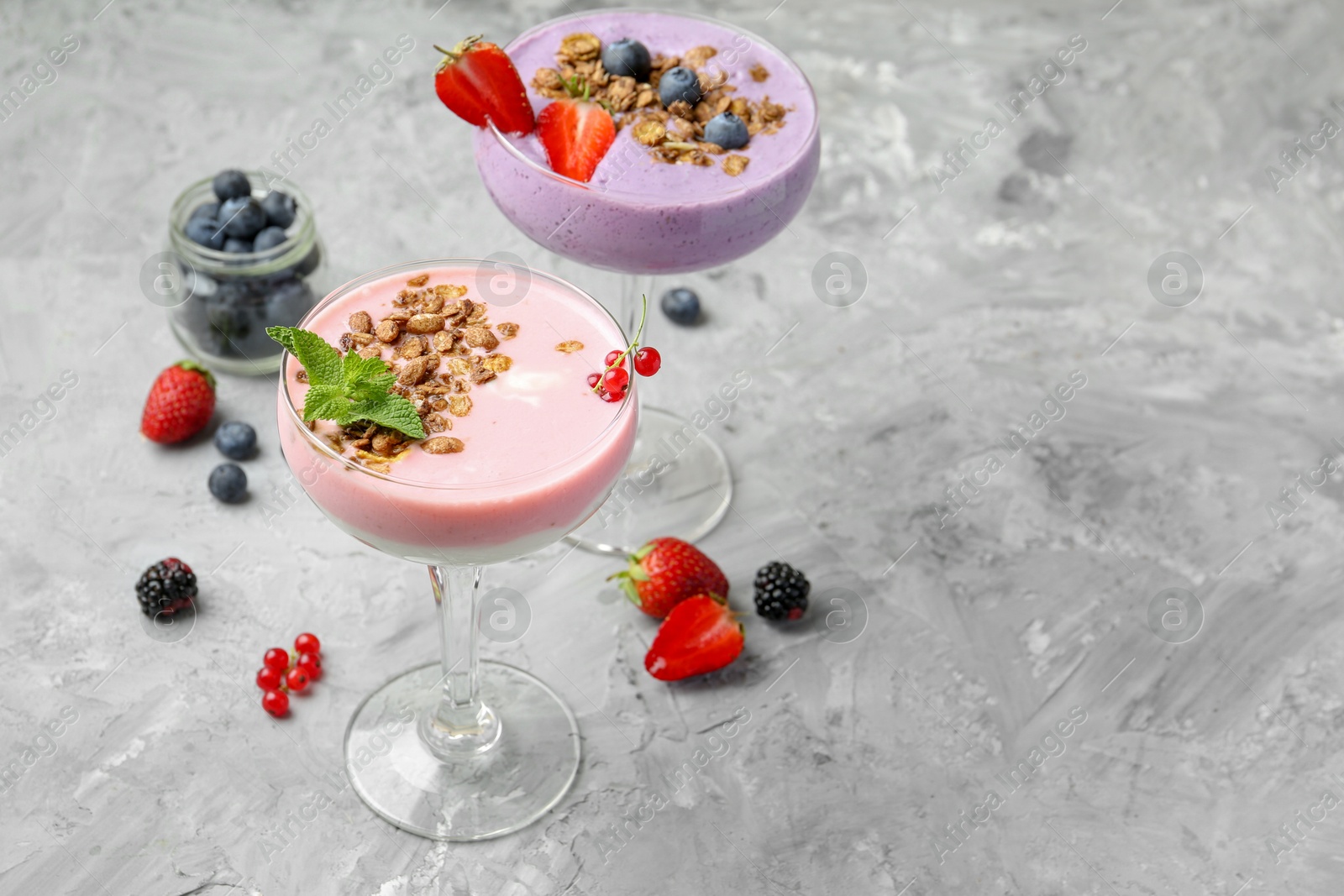 Photo of Different tasty yogurts with fresh berries and granola in glasses on gray textured table, space for text