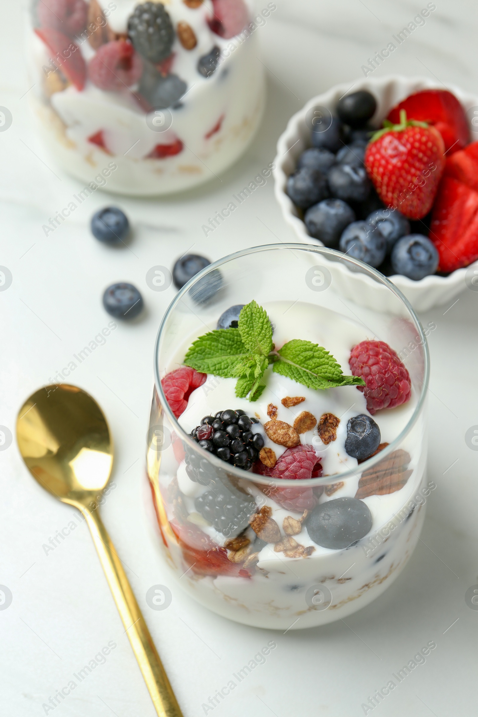 Photo of Tasty yogurt with fresh berries, granola and mint in glasses served on white table, closeup