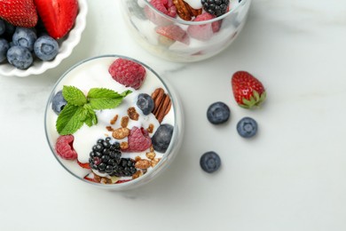 Photo of Tasty yogurt with fresh berries, granola and mint in glasses on white table, flat lay