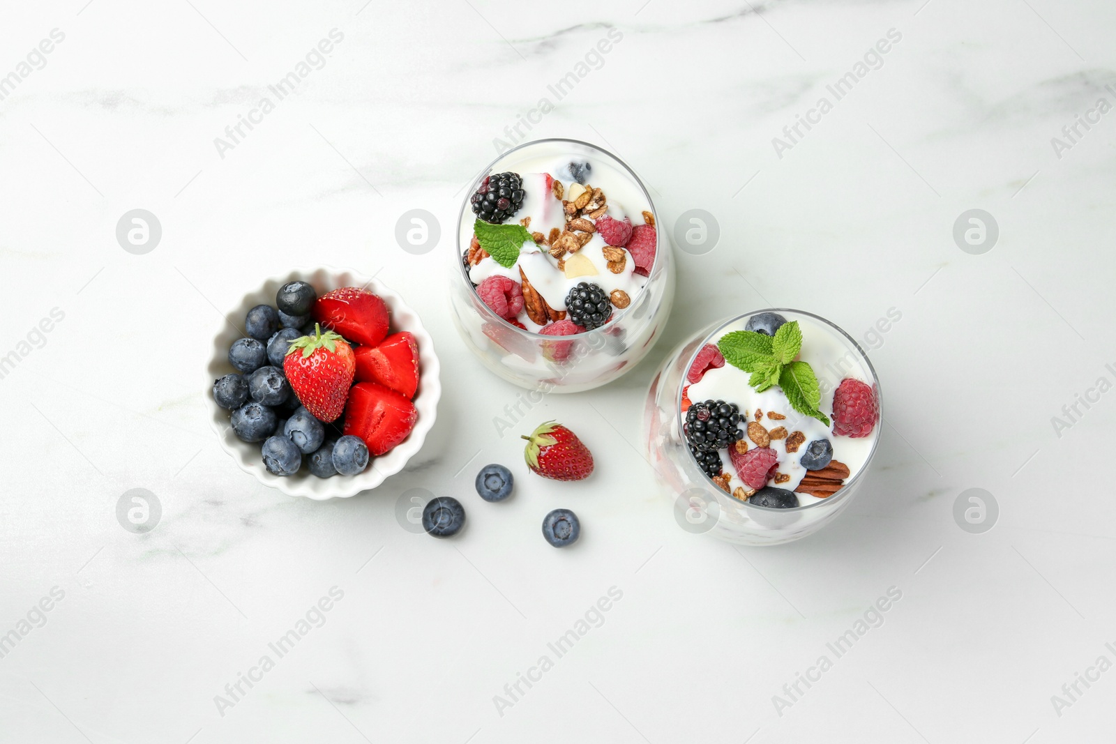 Photo of Tasty yogurt with fresh berries, granola and mint in glasses on white marble table, flat lay