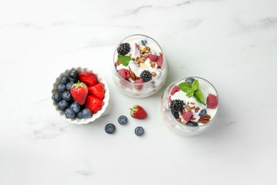 Tasty yogurt with fresh berries, granola and mint in glasses on white marble table, flat lay