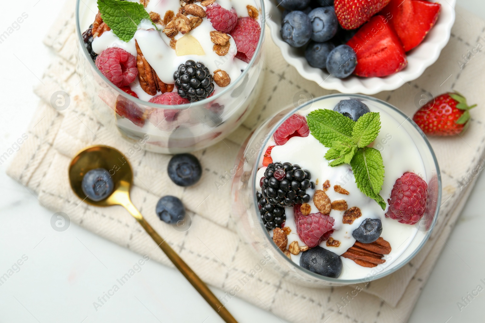 Photo of Tasty yogurt with fresh berries, granola and mint in glasses served on white table, flat lay