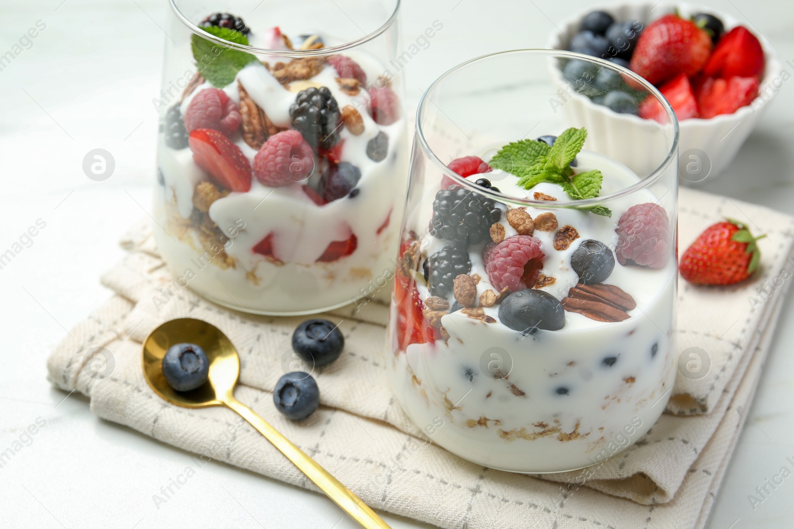 Photo of Tasty yogurt with fresh berries, granola and mint in glasses served on white table, closeup