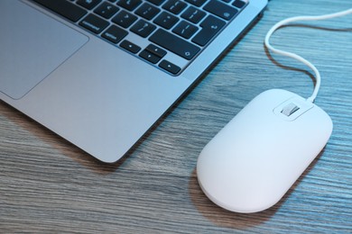 Photo of Computer mouse and laptop on wooden table, closeup