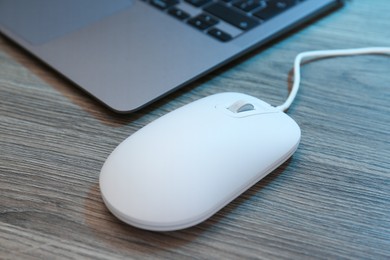 Photo of Computer mouse and laptop on wooden table, closeup