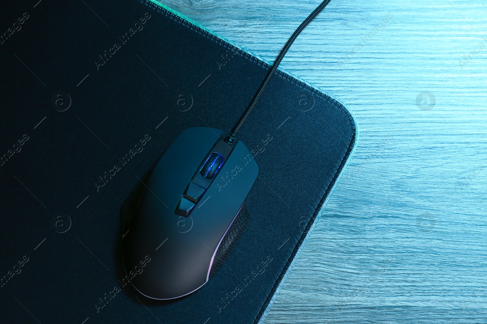 Photo of Computer mouse with mousepad on wooden table, top view