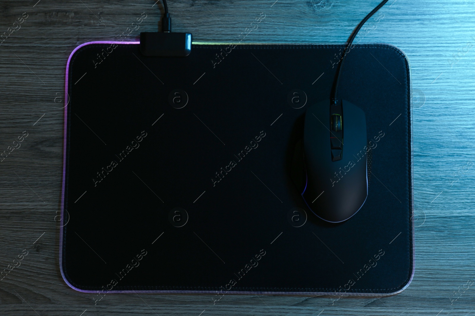 Photo of Computer mouse with mousepad on wooden table, top view