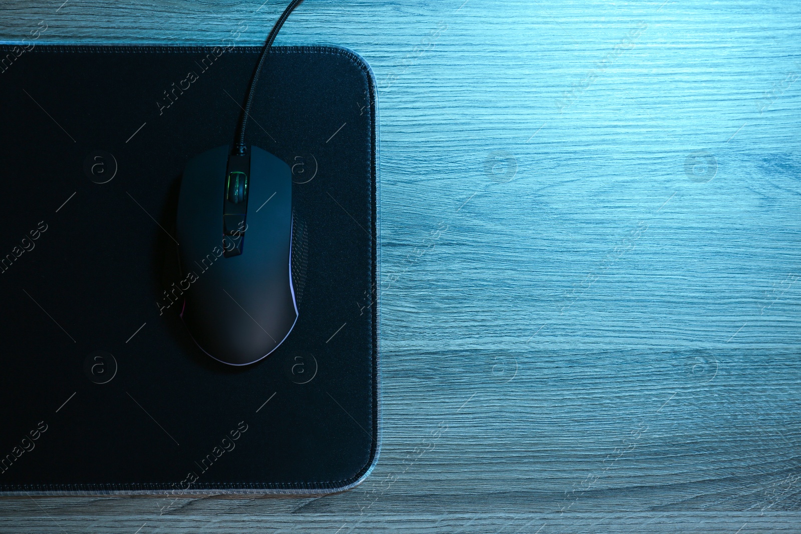 Photo of Computer mouse with mousepad on wooden table, top view. Space for text