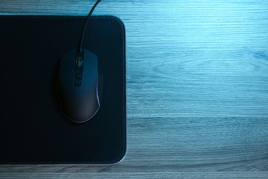 Photo of Computer mouse with mousepad on wooden table, top view. Space for text