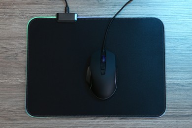 Photo of Computer mouse with mousepad on wooden table, top view